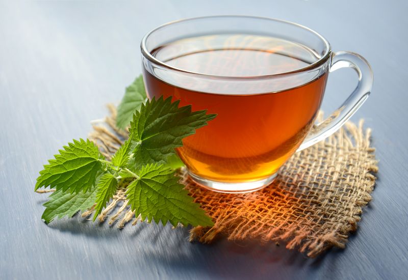 Taza humeante de infusión de jengibre junto a rodajas de raíz fresca sobre tabla de madera